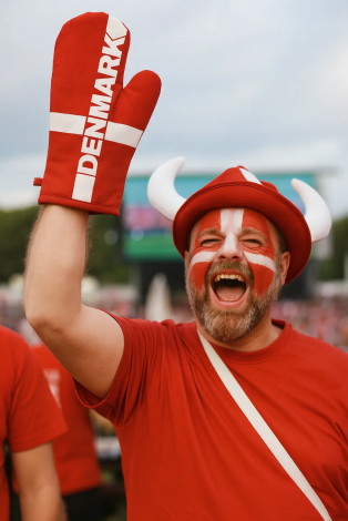 Mand iført ansigtsmaling og grillhandske med Dannebrog, der hepper på Danmark