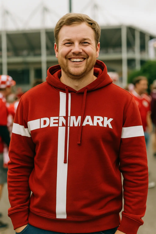 Glad mand iført en rød Danmark hættetrøje foran et stadion