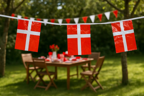 Dannebrogsguirlande i plast med røde og hvide flag hængende over havebord.