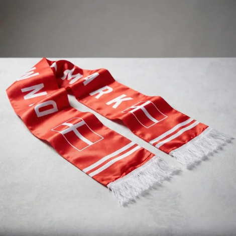 Et rødt satin halstørklæde med hvid 'DANMARK' tekst og hvide frynser, draperet på en lys overflade for at vise stoffets glansfulde kvalitet og tekstur
