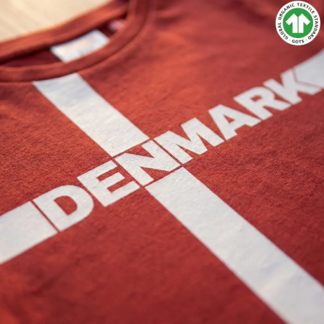 Nærbillede af brystkassen på en rød t-shirt, der viser den bløde tekstur af økologisk bomuld og det hvide kvalitetsprint med det danske flag og teksten DANMARK