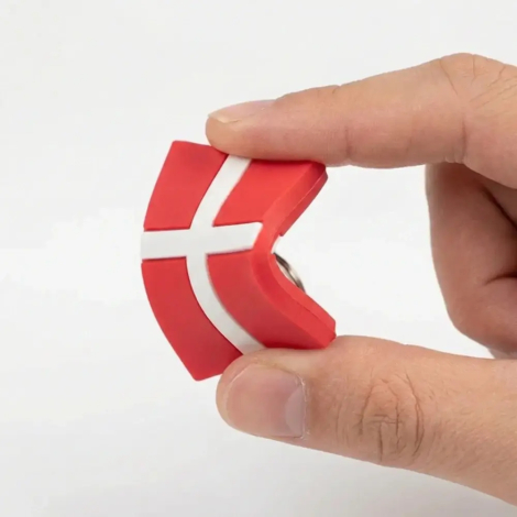 Nærbillede af en hånd, der bøjer en gumminøglering med det danske flag for at demonstrere materialets bløde og fleksible kvalitet