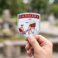 Hånd holder cykel og blomster klistermærke med Danmark tekst