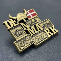 Nærbillede af en detaljeret, guldfarvet køleskabsmagnet i 3D-metal. Magneten danner ordet 'DENMARK' og er udsmykket med klassiske danske motiver som en vikingehjelm, Dannebrog, kongekrone, vikingeskib, en cykel og københavnske bygningsværker.